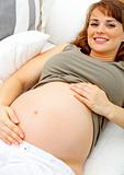 Smiling beautiful pregnant woman relaxing on couch and  holding her belly
