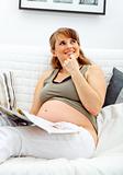 Dreaming beautiful pregnant woman relaxing on sofa with magazine.
