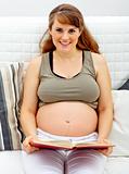 Smiling beautiful pregnant woman sitting on sofa with book
