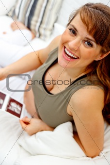 Happy beautiful pregnant woman relaxing on sofa and holding  echo in hands.
