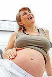 Laughing beautiful pregnant woman relaxing on sofa and  holding her belly
