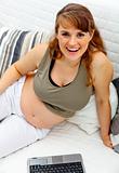 Pleased beautiful pregnant woman sitting on sofa with  laptop
