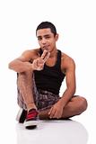 Young latin man, sitting on floor, with thumb raised as a sign of victory, isolated on white background. studio shot