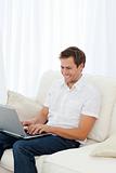 Man laughing while working on his laptop on the sofa