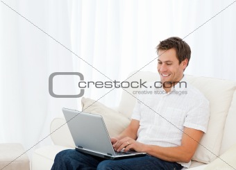 Handsome man working on his laptop while relaxing on the sofa