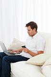 Positive man buying online sitting on his sofa
