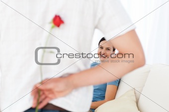 Attentive man hidding a flower behind his back for his girlfriend