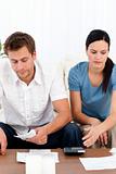 Desperate couple looking at their bills sitting on the sofa