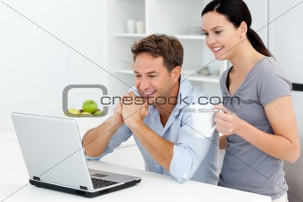 Happy couple looking at something on the laptop while drinking 