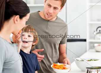 Little boy giving his mother a carrot while preparing lunch