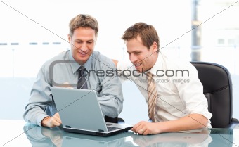 Two happy businessmen working together on a laptop sitting 