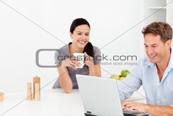 Cheerful couple looking at something on internet while drinking 