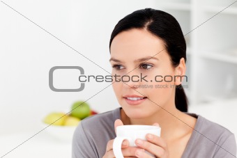 Pensive woman holding a cup of coffee sitting in the kitchen