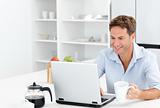 Happy man working on his laptop while drinking coffee