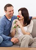 Cute woman smelling a red rose while relaxing on the sofa