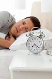 Unhappy man looking at his alarm clock while lying on his bed