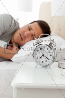 Unhappy man looking at his alarm clock while lying on his bed