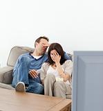 Scared couple hiding their faces while watching a horror movie