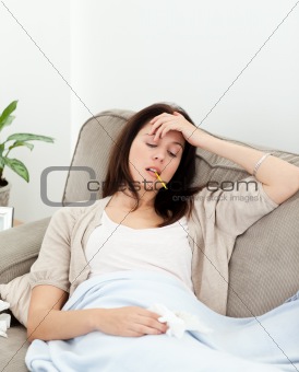 Sick woman taking her temperature with a thermometer on the sofa