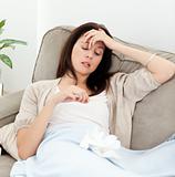 Sick woman looking at a thermometer while resting on the sofa