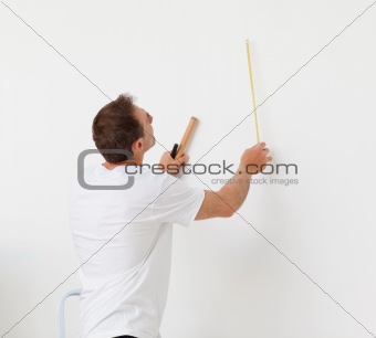 Handsome man looking at a wall with ruler and tools