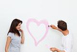 Cute woman looking at her boyfriend painting a heart