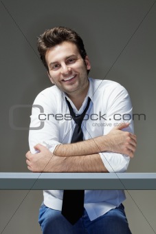 businessman in shirt, tie and jeans sitting at desk, smiling - isolated on gray