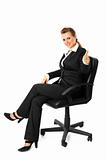 Smiling modern business woman sitting on chair and showing thumbs up gesture

