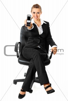 Smiling modern business woman sitting on chair and showing mobile phone in hand
