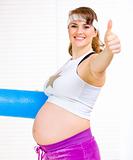 Smiling beautiful pregnant woman with exercise mat showing thumb up gesture
