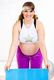Smiling beautiful pregnant woman holding exercise mat in hands
