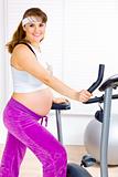 Smiling beautiful pregnant woman preparing for workout on static bike
