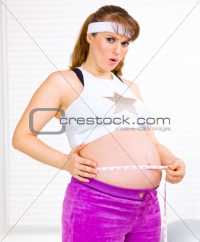 Surprised beautiful pregnant woman measuring her tummy
