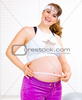 Smiling beautiful pregnant female measuring her belly
