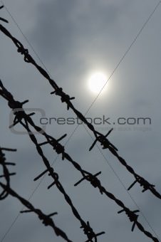 Barbed wire on a background of the sky and the sun