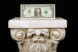 The Almighty Dollar - One dollar bill on a pillar with a black background.