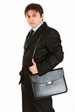 Serious young businessman holding briefcase on shoulder
