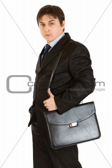 Serious young businessman holding briefcase on shoulder
