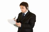 Serious young businessman with headset and making notes in document

