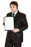 Serious young businessman with headset holding blank clipboard
