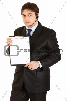 Serious young businessman with headset holding blank clipboard
