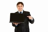 Smiling modern businessman pointing finger on laptops blank screen
