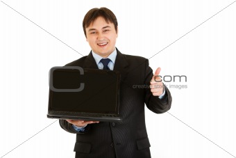 Smiling modern businessman holding laptops blank screen and showing  thumbs up gesture
