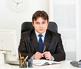 Serious modern businessman looking at camera sitting in office
