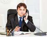 Thoughtful modern businessman talking on phone and making notes in diary
