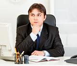 Pensive young businessman sitting at desk and planning timetable in diary
