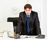 Strict modern businessman standing at office desk
