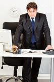 Strict modern businessman standing at office desk
