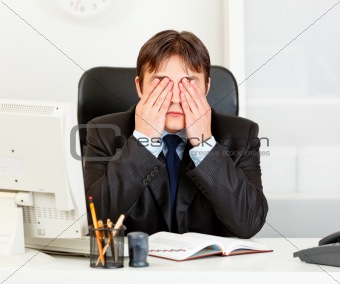 Modern businessman sitting at office desk and making see no evil gesture
