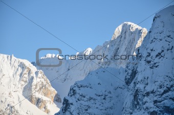 Snowcovered mountain peak with cross on top.